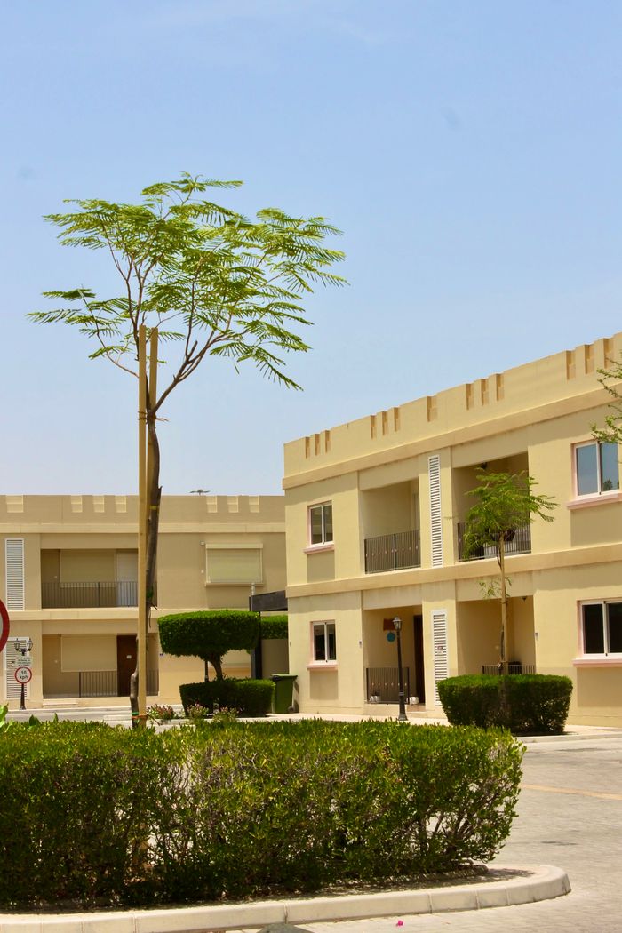 Contact Sunny day view of a modern apartment complex with greenery and clear blue sky.