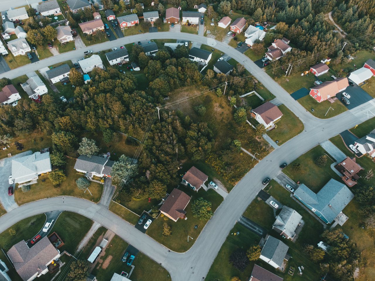Services Aerial shot of a suburban neighborhood with houses and lush greenery, captured during the day.